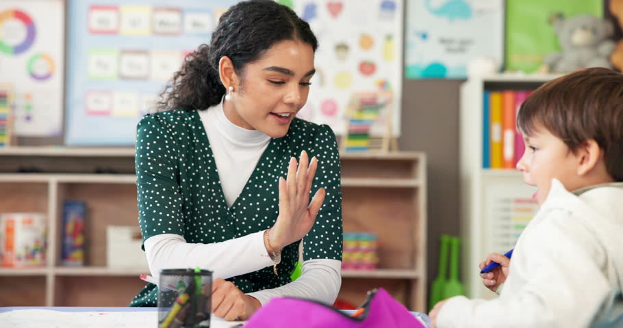 Education, high five or study with student and teacher in classroom together for development. Conversation, success or teaching with boy child and woman at desk in school for academic scholarship