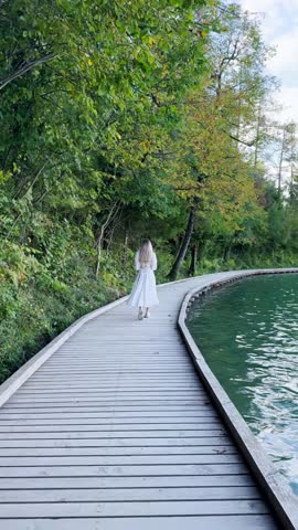 Woman Walking Along a Wooden Path by the Lake – Stunning Views and Sunny Adventure