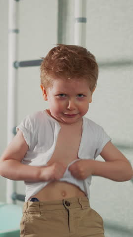 Naughty little boy tears white t-shirt on chest playing action movie hero slow motion. Toddler kid destroys clothes in home gym. Angry child emotions