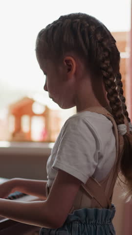 Kid musician plays piano looking at sheet music. Balanced child with limited mobility does hobby standing in light room at home on blurred background slow motion