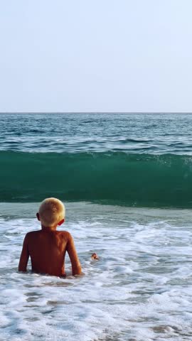 A child catches waves while sitting on the sand in the Mediterranean Sea at sunset. A boy in the sea on the beach in Alanya. A foaming wave. A child's delight in relaxing at sea. Turkey.4K