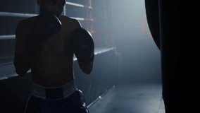 Focused African American man with bare torso punches hanging bag near ring. Bearded black sportsman exercises beating equipment in professional gym of club - Powered by Shutterstock - Get 15% off with code: PIKWIZARD15
