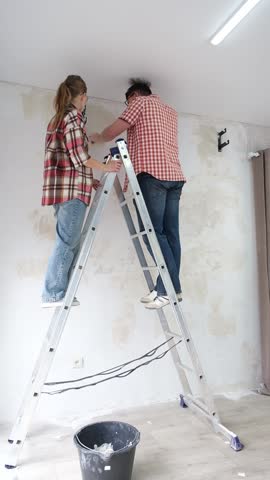 couple renovating new house apartment , spackling wall, woman holding a bucket on ladder . Home makeover, renovation concept. Family man woman repair house themselves. vertical video