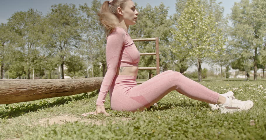 Young woman performs calisthenics exercises in a park. She is determined and focused on her fitness routine.