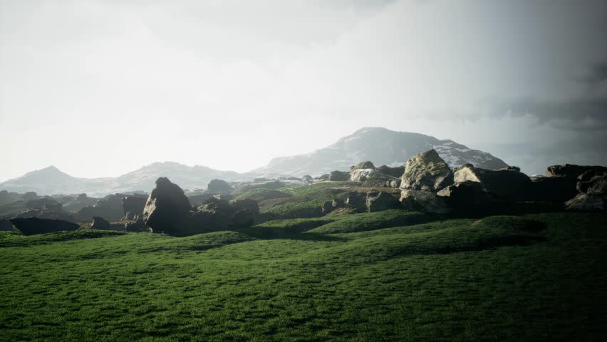 A tranquil landscape with majestic mountains, rugged rocks, and vibrant green grass under a cloudy sky