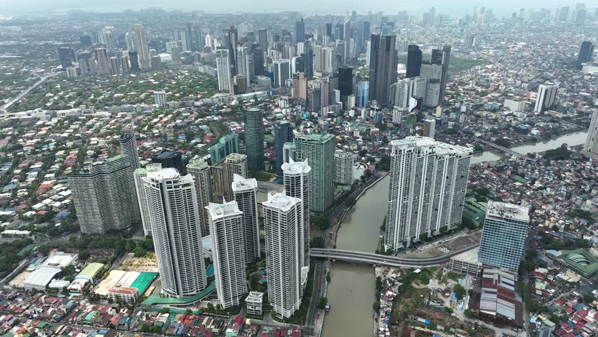 Manila cityscape at river banks aerial. Downtown area with cottages, skyscrapers, buildings. Urban Philippines city scape with streets and roads. Town drone shot. Poor Homes Along Rich Skyscrapers.