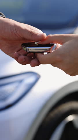 Vertical Video of Female hand gives a car keys to male hand in the car dealership. Auto seller and a man who bought a vehicle shake hands. Dealer giving key to new owner in auto show or salon.