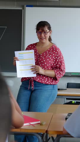 Vertical HD video of young elementary school teacher explaining exercises to her pupils at school. 10 year-old students studying in class. Grade school and education concept.