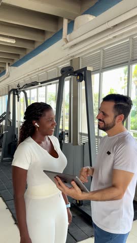 Fitness instructor explaining workout routine to client using tablet in gym