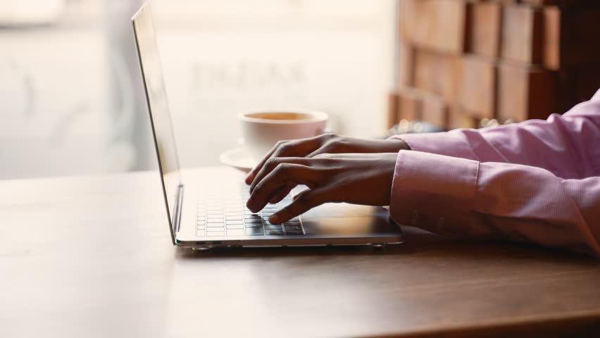 Close-up of hands typing on laptop at cafe table