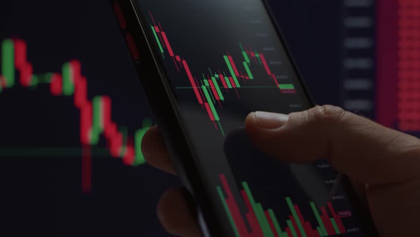 Close up of trader hand holding smartphone, using trading app with stock market charts for financial analysis and monitoring investment data. - Powered by Shutterstock - Get 15% off with code: PIKWIZARD15