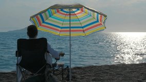 Woman relaxing on beach chair under umbrella enjoying ocean view. Mature female relaxing on beach chair under vibrant beach umbrella, while gazing at sparkling ocean waves and coastal landscape - Powered by Shutterstock - Get 15% off with code: PIKWIZARD15
