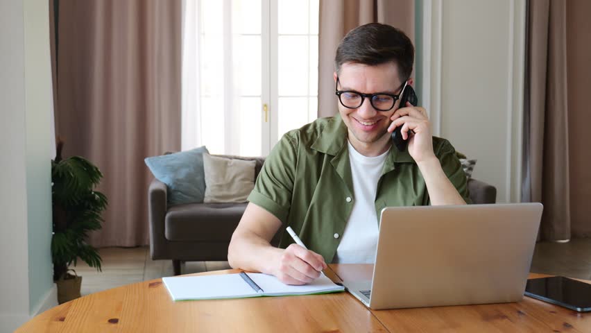 Focused Individual Engages in a Phone Conversation While Working on a Laptop in a Bright, Modern Workspace