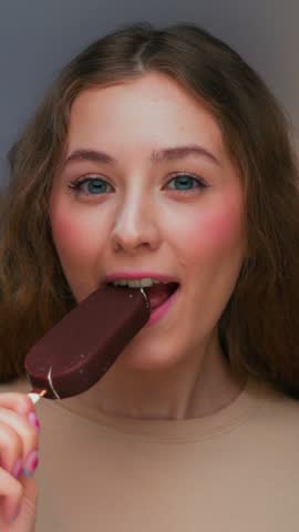 Portrait of Young Woman Eating Sweet Food as Looking at Camera. Real Person on Diet Consuming Milk Ice Cream as Lunch Snack. Attractive Female Human Inside Cozy Living Room Alone with Sugary Milky Bar