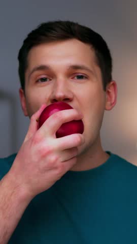 Portrait of Adult Man Eating Healthy Food as Looking at Camera. Real Person on Diet Consuming Fresh Red Apple as Quick Lunch Snack. Confident Male Human Inside Cozy Living Room Alone with Organic Meal