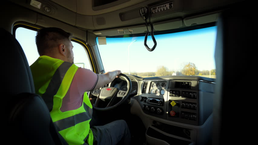 Professional Semi Truck Driver wearing a safety vest is riding a truck on beautiful sunny day. Shot from inside the truck