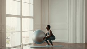 In a bright indoor space, a woman raises a stability ball above her head while engaging in a fitness routine. She maintains a fit and athletic appearance, promoting a healthy lifestyle. - Powered by Shutterstock - Get 15% off with code: PIKWIZARD15