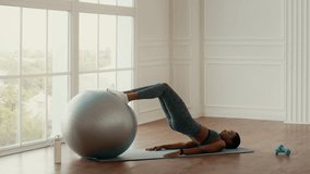 An African American woman engages in a workout session at home, using a stability ball for core strength training. The bright indoor space is designed for a healthy lifestyle. - Powered by Shutterstock - Get 15% off with code: PIKWIZARD15