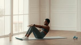 A young African American woman performs abdominal exercises on a workout mat at home. She maintains focus, showcasing dedication to her fitness routine in a bright indoor space. - Powered by Shutterstock - Get 15% off with code: PIKWIZARD15