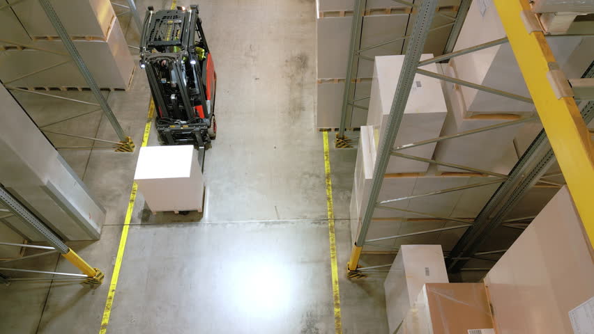 A forklift navigates an aisle in a warehouse, lifting a large box, highlighting efficient storage and distribution logistics.