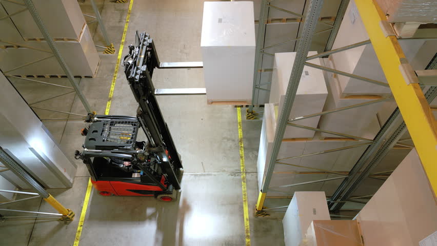 A forklift navigates an aisle in a warehouse, lifting a large box, highlighting efficient storage and distribution logistics.