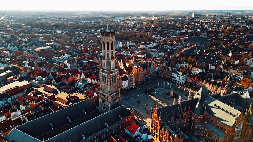 Bruges showcases its iconic medieval architecture, including the Belfry tower and bustling squares filled with visitors enjoying the beautiful view in a sunny setting.