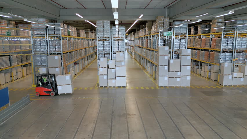 A vast warehouse with high ceilings and metal racks filled with goods. A forklift navigates the aisles, highlighting the efficient storage and logistics system.