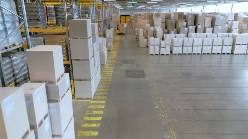 A top-down view of a warehouse reveals a black autonomous forklift navigating between rows of stacked boxes, highlighting efficient logistics and automation in a vast storage facility.