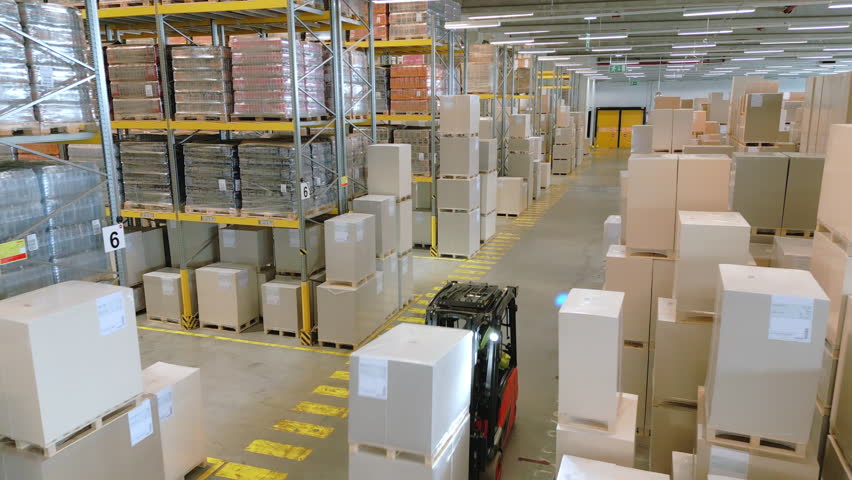 A vast warehouse reveals rows of stacked boxes and crates, highlighting efficient storage and distribution logistics. The overhead shot emphasizes the organized layout and scale of the facility.