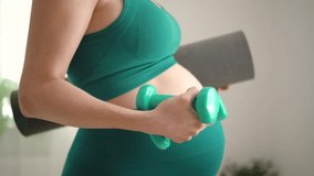 A pregnant woman prepare for exercising with dumbbells. Young girl holding a yoga mat in hand. Concept of a healthy lifestyle during pregnancy. Sports activities before the birth of baby. - Powered by Shutterstock - Get 15% off with code: PIKWIZARD15
