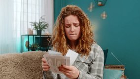 Young woman at home holding bills and receipts with head in hands looking sad and stressed by expenses. Caucasian redhead girl on sofa feeling emotional pressure, financial trouble and disappointment - Powered by Shutterstock - Get 15% off with code: PIKWIZARD15
