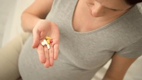 Pregnant woman holding a pill in one hand and touching her head with the other. Top view close-up showing headache and need for relief. - Powered by Shutterstock - Get 15% off with code: PIKWIZARD15