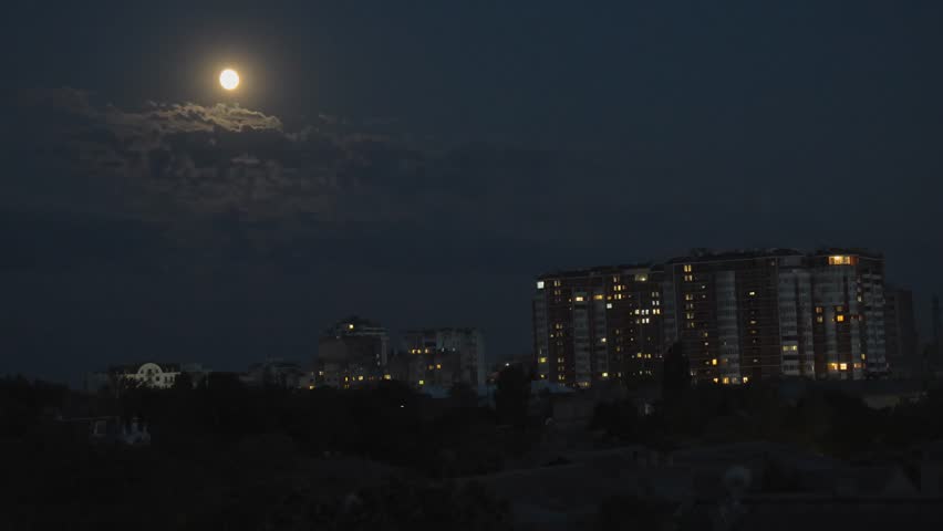Bright full moon glowing through scattered clouds above a cityscape with illuminated apartment buildings and dark silhouettes of trees in the foreground - Powered by Shutterstock - Get 15% off with code: PIKWIZARD15