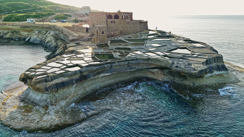 On the coast of Malta, the aerial perspective reveals expansive salt pans alongside a historic structure, highlighting the island's rich culture and natural beauty.