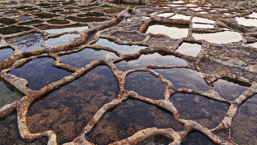An aerial view captures the intricate design of Malta's salt pans. Natural pools reflect the sky, showcasing the artistry of this traditional harvesting method.