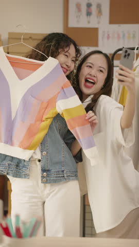 Asian woman influencer live streams a fashion product showcase from studio. Two female SME Online store business owner selling clothes on social media. entrepreneur, e-commerce, side hustle concept.
