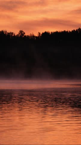 Bright orange sunrise over river and forest. Beautiful morning landscape. Nature background. Vertical video