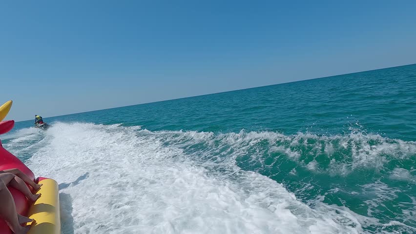 People ride banana boat at speed during summer vacation on blue sea. Water scooter rides on water attraction banana. Water entertainment. Travel