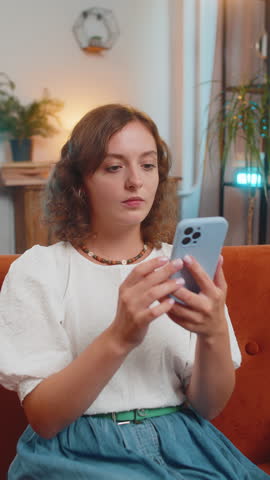 Happy excited young woman using smartphone typing browsing found out great win good news celebrate victory. Amazed Caucasian girl with mobile phone sitting at home apartment on sofa. Wow emotion