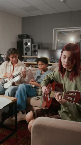 Vertical view of two African American teenage siblings rehearsing song with Caucasian girl playing acoustic guitar in music studio