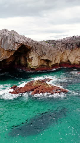 Raging blue sea water splashes by the rocks. Unapproachable mountains surround the waterscape. Vertical video.
