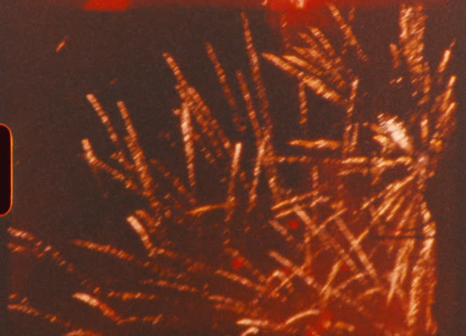 Retro 8mm footage showcasing bright orange fireworks exploding against midnight backdrop, displaying luminous patterns with classic film texture and grainy aesthetic
