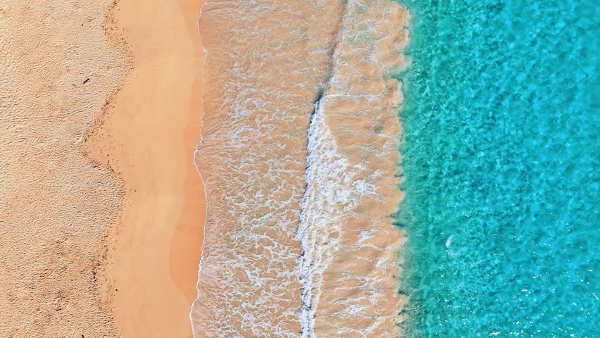 Top view of waves crashing on sandy beach. Empty tropical beach and seascape. Ocean and coast. Summer vacation in the tropics. Sea wave with foam rolling onto the shore.