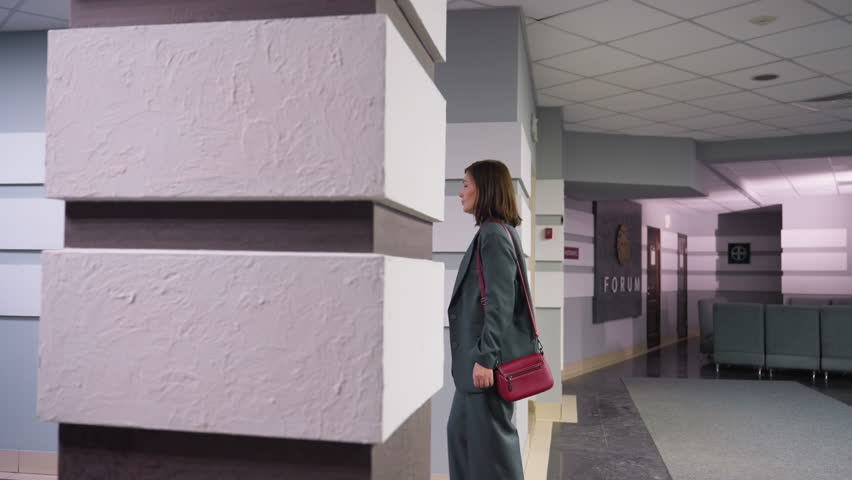 Modern office hallway with minimalist wall design, textured panels, and distant lounge area featuring grey couches and corporate doors, creating a professional and contemporary workspace atmosphere