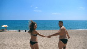 Happy couple holds hands of each other running on sandy beach to the sea. Young smiling lovers jogging to seaside at sunny day. Cheerful man and woman having fun together at seashore. Vacation concept - Powered by Shutterstock - Get 15% off with code: PIKWIZARD15