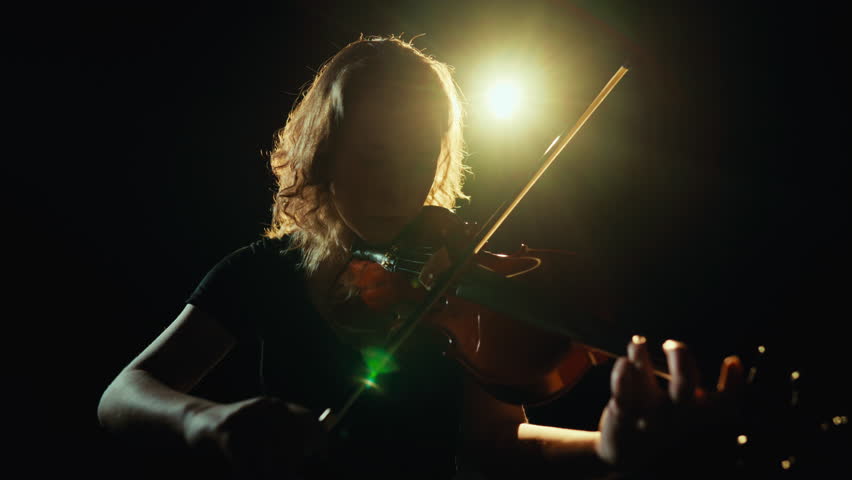 Self-expression by musical instruments play, young adult lady playing violin. Romantic mood and enjoy concert of classical music in modern theatre, professional musician rehearsing in dark studio