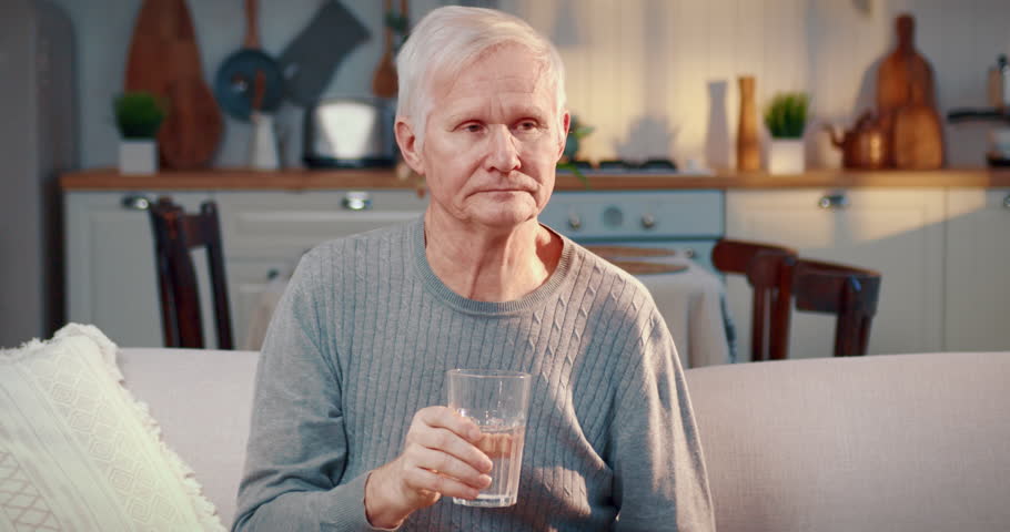 Elderly man drinking water from glass at home, healthy lifestyle, body hydration . Portrait of aged male person in living room, healthy nutrition and diet for lose weight, curing disease by hungry
