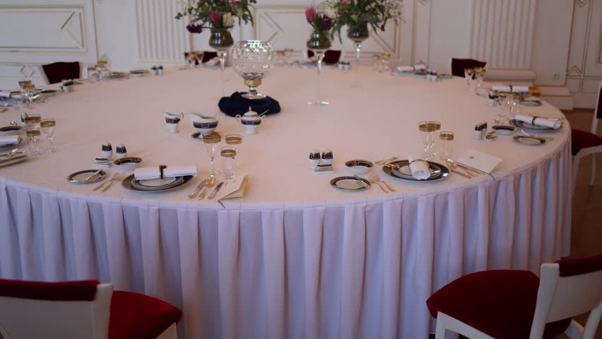 A royal round table set for an elegant gathering. Fine porcelain, gold-rimmed glasses, and floral centerpieces create a luxurious atmosphere ready for a grand dining experience.