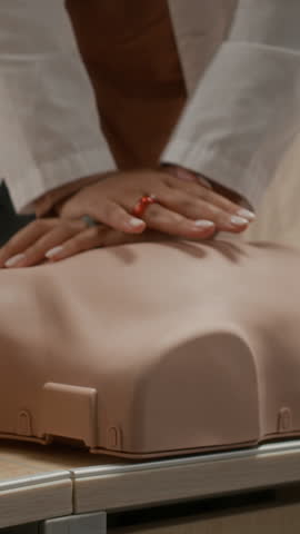 Vertical tilt up shot of smiling Black teenage girl practicing CPR technique on manikin in training class for medical students at college