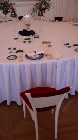 Vertical screen elegant round table set with fine china and gold-rimmed glasses in classic interior red velvet chair soft florals luxury dining setup